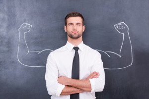 Handsome young man in shirt and tie looking at camera and keeping arms crossed while standing against chalk drawing of muscular arms