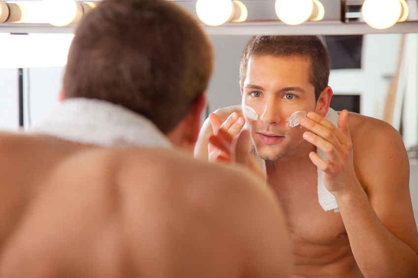 Young man shaving in bathroom mirror